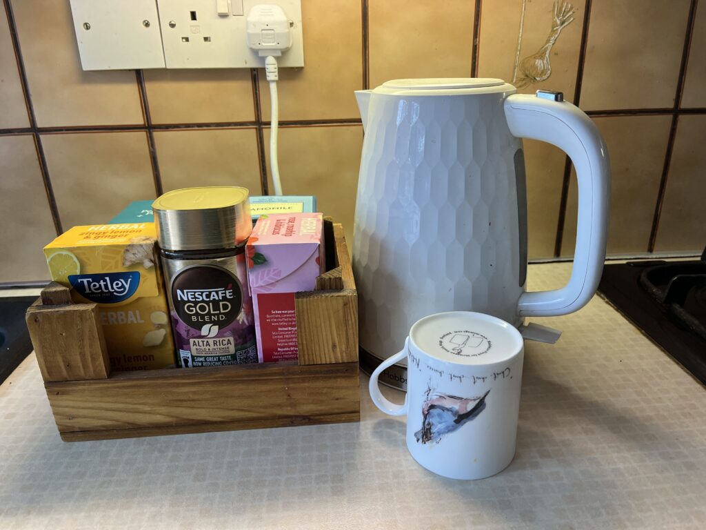 Compact wooden mini crate on a kitchen counter, organised with a selection of hot beverage supplies including Tetley herbal tea, NESCAFÉ GOLD coffee.